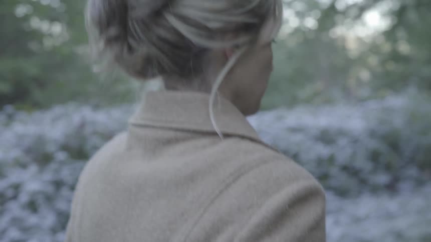 A woman with her hair up in a twist walks through a park wearing a heaving coat