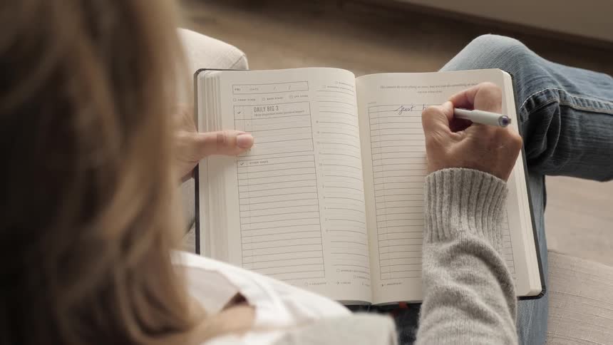A woman sits with her leg crossed over the other and writes in a diary