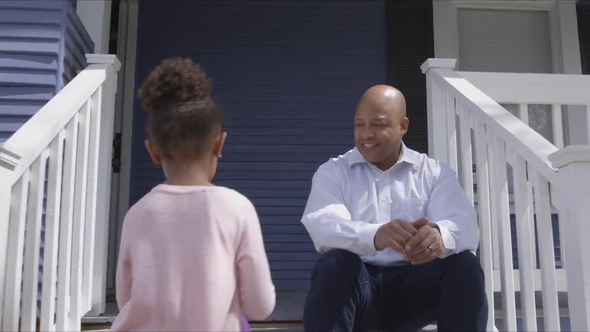 Girl goes up to a man's side to sit with him at the doorstep on a sunny day