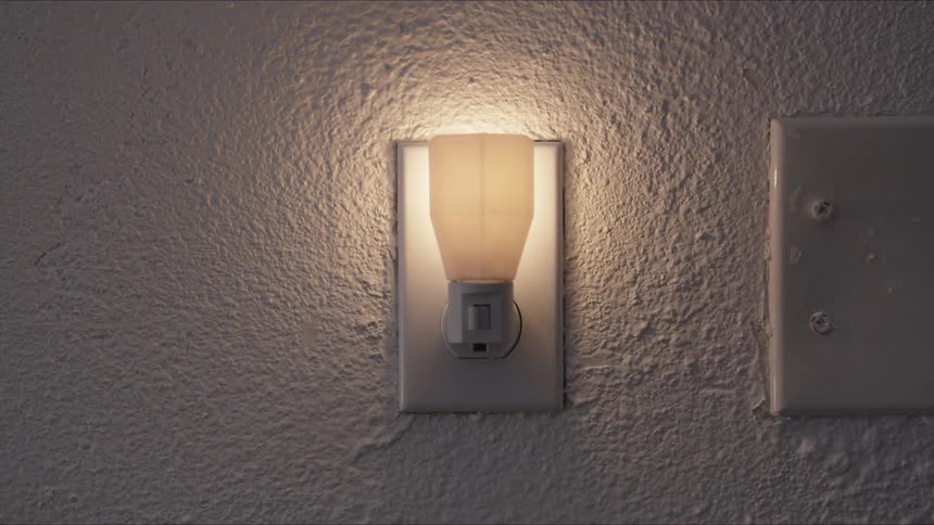 A man plugs in a nightlight in a dim lit room