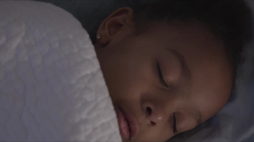 A girl laying in bed covered in a blanket with her eyes closed