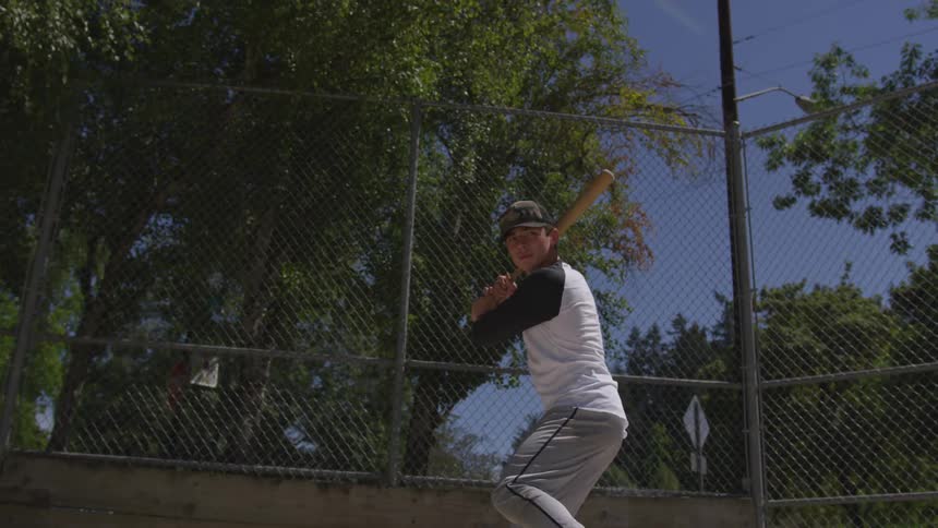 Baseball player pretends to hit baseball with baseball bat in hand on a sunny day
