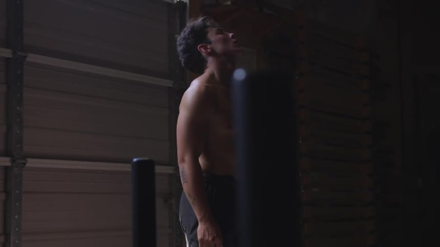 A muscular man without a shirt stretches his neck as he stands upright