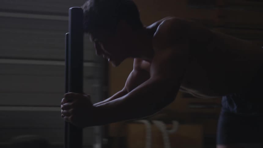 A shirtless man pushing a cart of weights in a gym