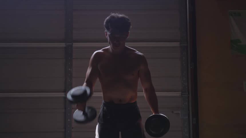 Man lifts dumbbells in a dark dim room