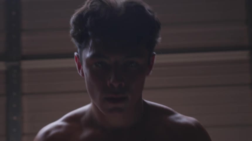 A young shirtless man lifts dumbbells