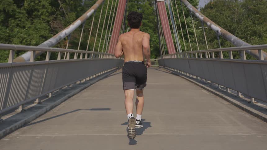 Shirtless man jogging on a bridge
