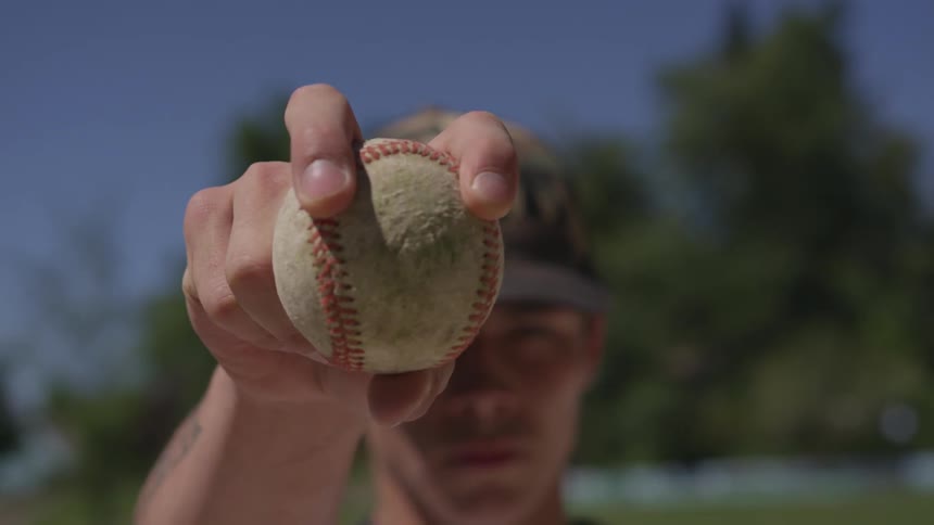 A man wearing a hat holds up a baseball