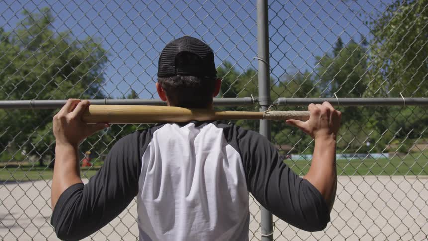 Person looks at baseball field through fencing while holding bat