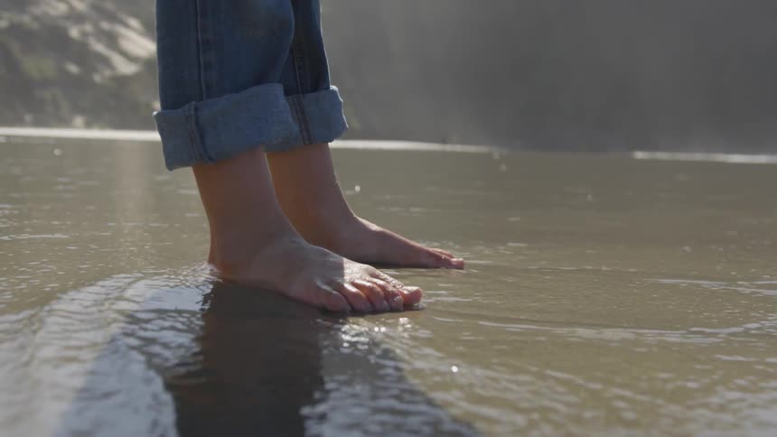 Person standing barefoot on the wet shoreline