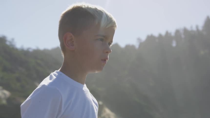 A blonde boy stands outside on a sunny day