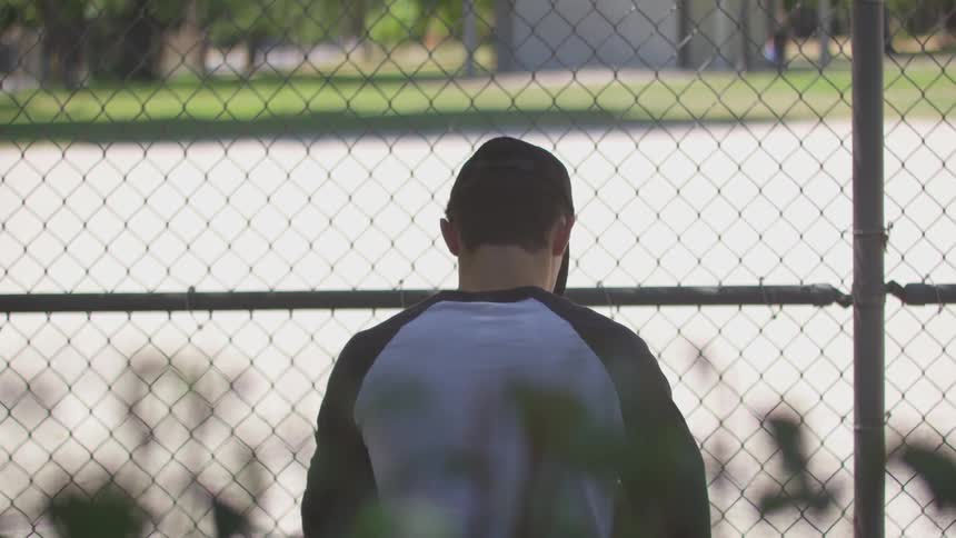 Teenage boy stands outside a baseball field and plays with a ball and glove