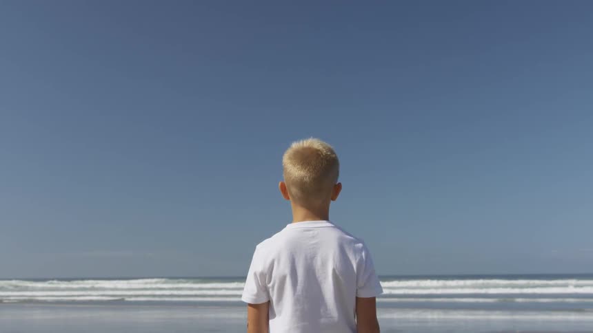 A boy in a white shirt staring at the ocean