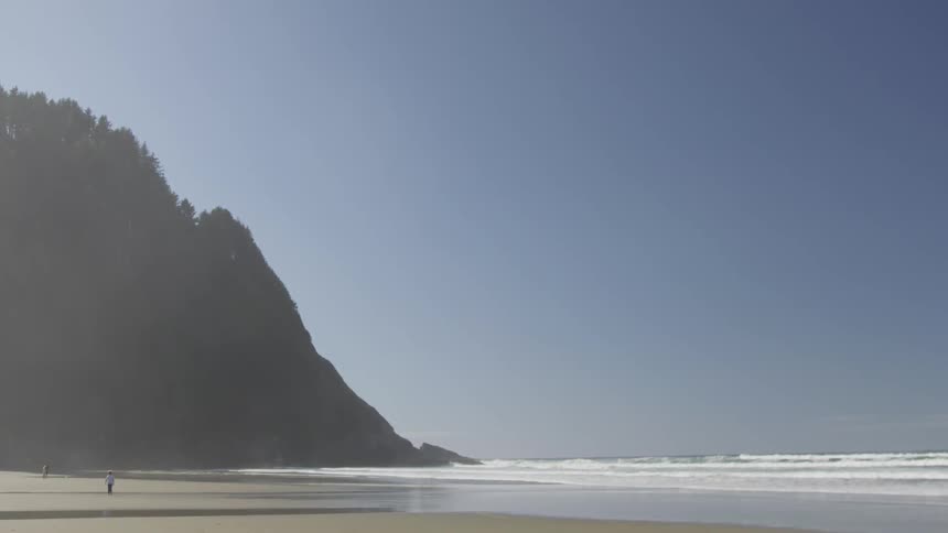 Far away people walk down a sunny beach next to a hill