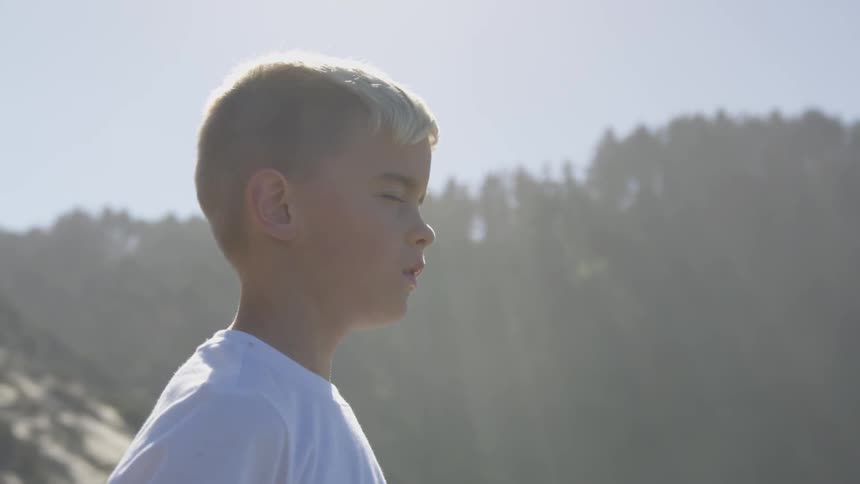 A child stands in nature with his eyes closed