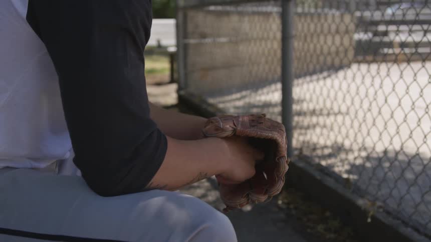 A man sits down as fidgets with a baseball in the park at day