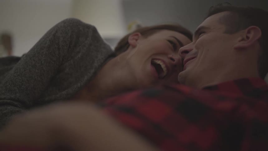 Couple laying in bed on bedroom laughing and talking