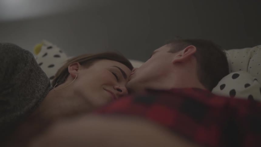 A man kissing a woman on her forehead laying in bed