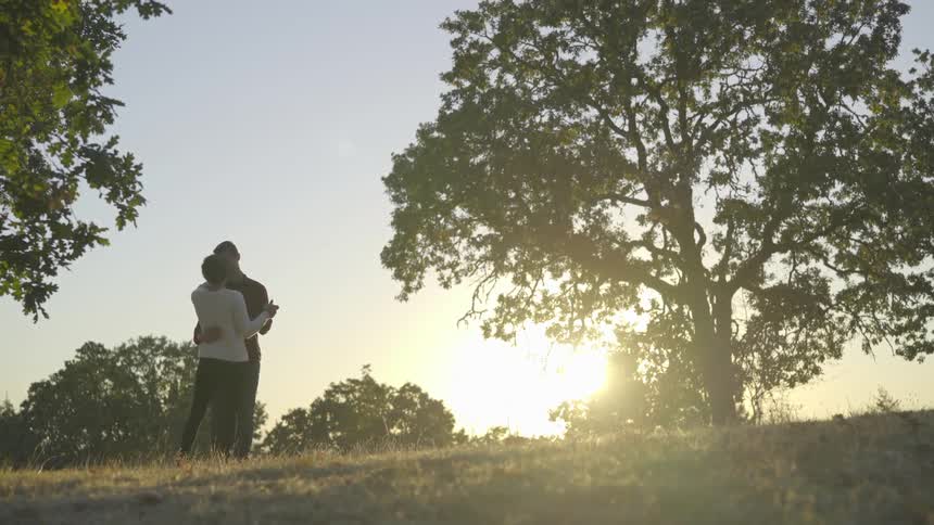 A man and woman are dancing on the top of a grassy hill