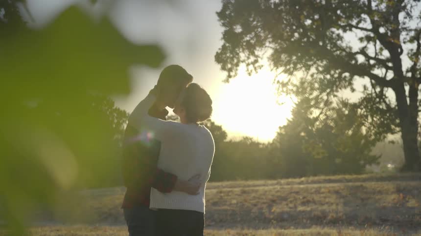 Couple slow dances outdoors in field near trees at sunset