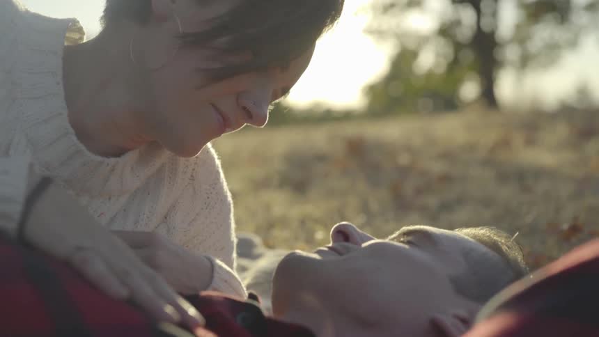 Woman leans over man as they lay on grass