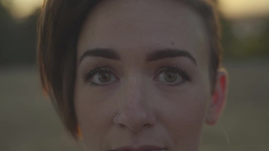 A woman with a short edgy haircut and nose ring turns her head