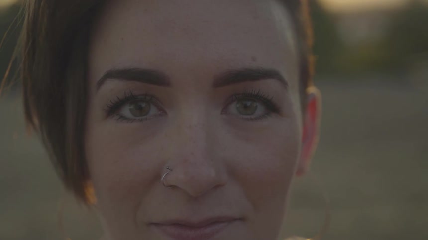 A woman with a nose ring looks to the side and then smiles