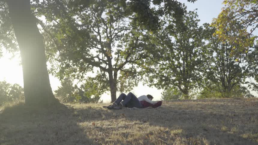 A couple lies in the grass under the large tree