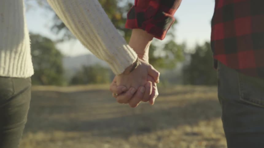 Man and woman hold hands while walking on the grass