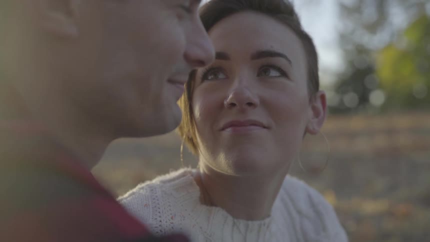 A woman turns her head and looks lovingly at her man while sitting outside in the grass