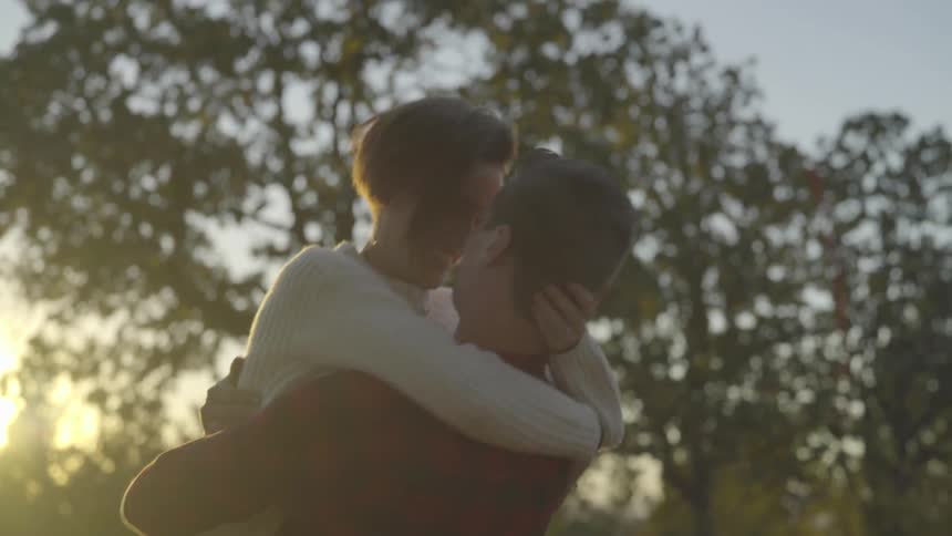 Man picks up woman and hugs her in a field at sunrise
