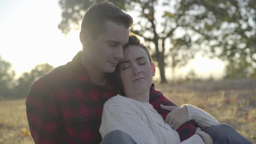 A woman sitting in the embrace of a man in field during the day