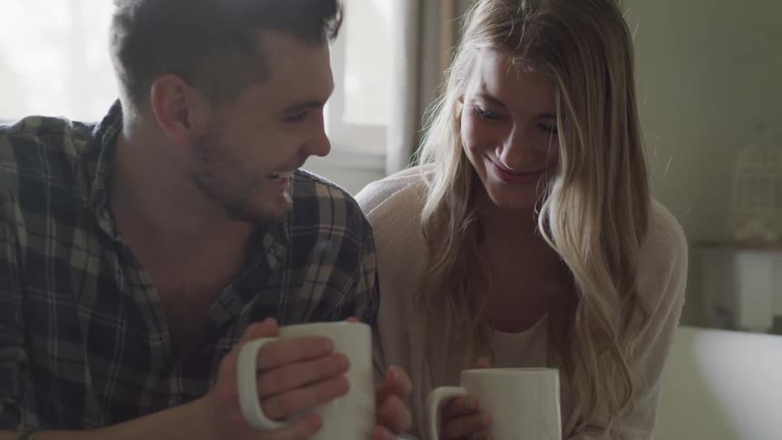 A man and a woman drinking steaming drinks together on a couch