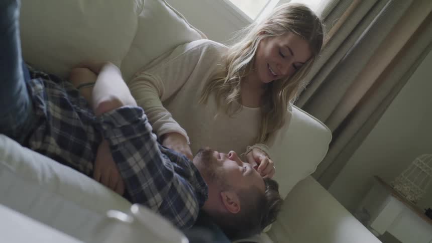 A woman strokes a mans hair as he lays his head on her lap on the couch