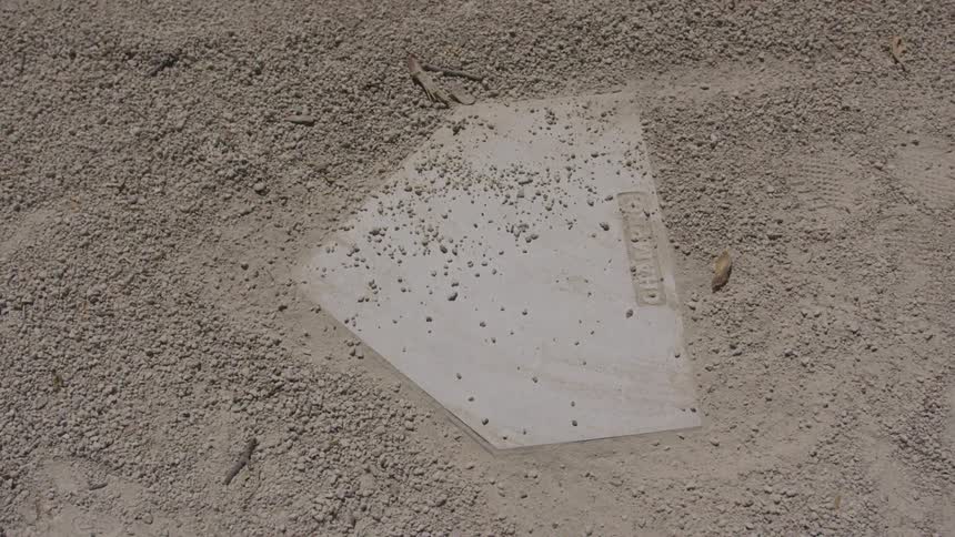 Circling a home plate partially covered with sand that is marked with imprints of shoes
