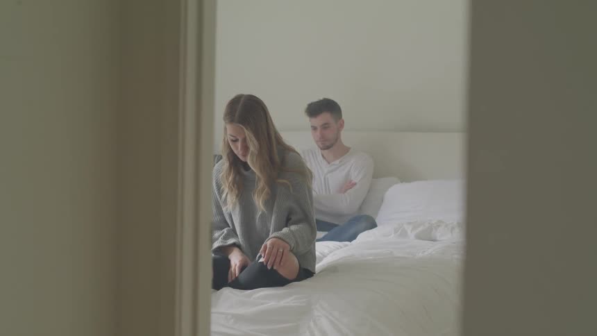 Couple sitting on bed in bedroom silently