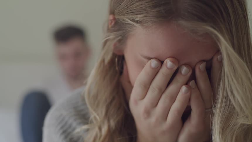 Young woman covering face with hands with man in background