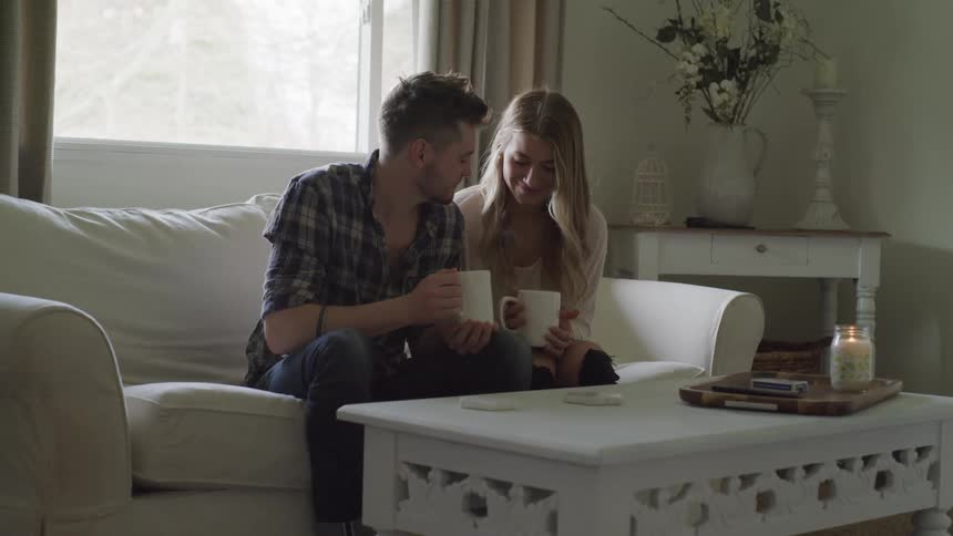 A man and woman sit together on a couch drinking coffee