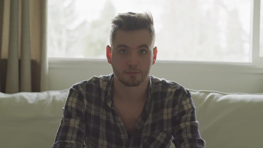 A man raises his head from a lowered position sitting on a couch