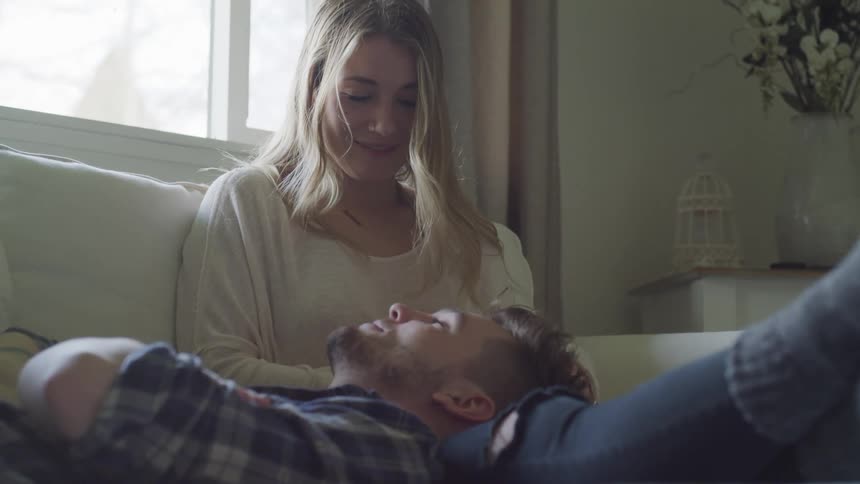 Woman sits on couch with man's head in her lap