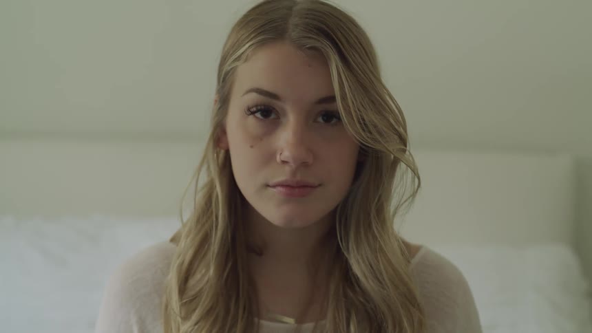 A woman is sitting on a bed and lifts her head upward