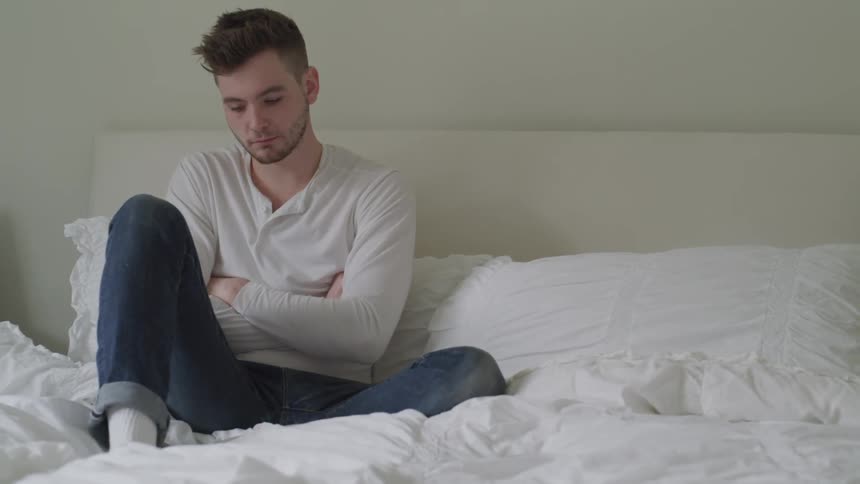 A man sits on a bed crying and shaking his head