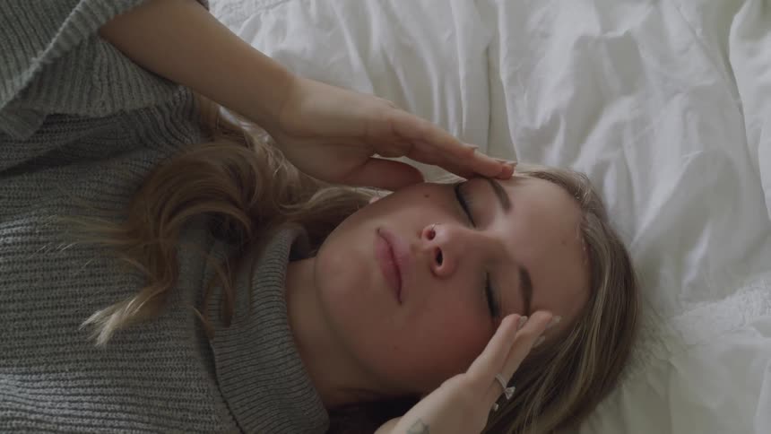Woman lays back on bed rubbing temples
