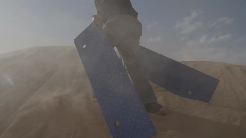 Man carries large pieces of metal through a windy desert