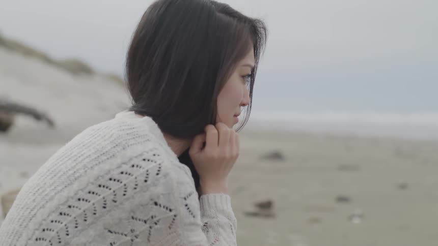 A woman sits on the beach distraught