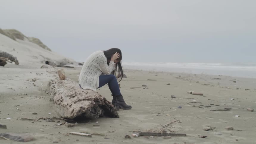 Woman sits on rock on beach