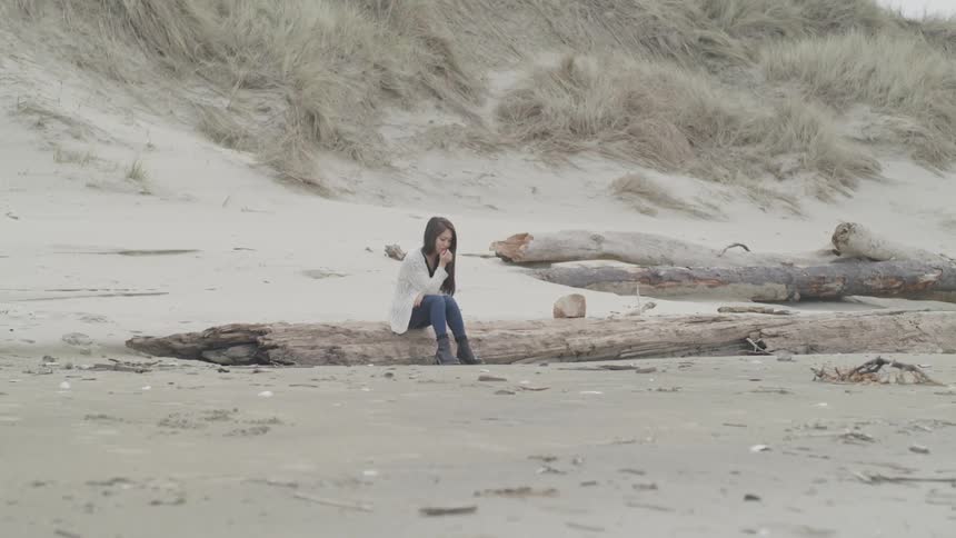 A sad woman sits on a log on a sandy beach