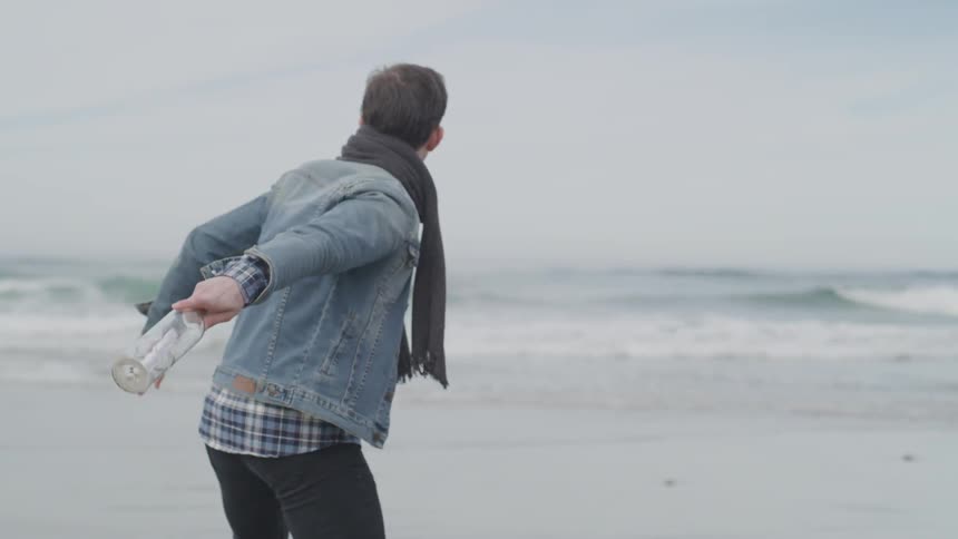 A man throws a glass bottle with a message in it into the ocean waves