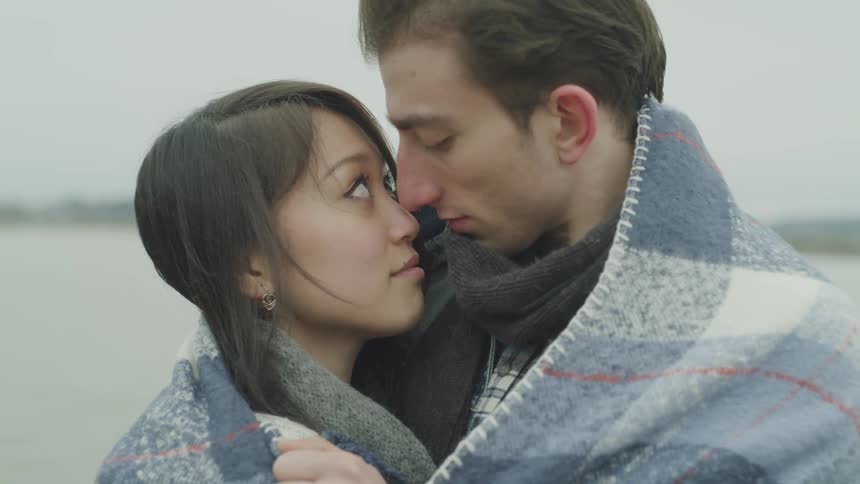 A young couple look into each others eyes longingly as they are wrapped in a blanket