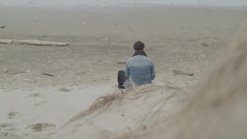 Man sits in sand at base of hill